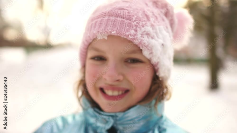 Close portrait of a girl in a snowy pink hat after a snow fight in the park. The child smiles cheerfully Close portrait of a girl in a snowy pink hat after a snow fight in the park. The child smiles cheerfully