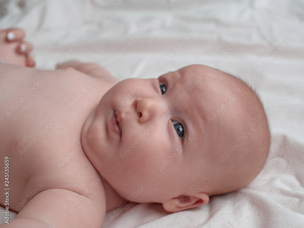 Baby with playful and flirting facial expression. The baby lies on a white linen cloth. Baby with playful and flirting facial expression. The baby lies on a white linen cloth.