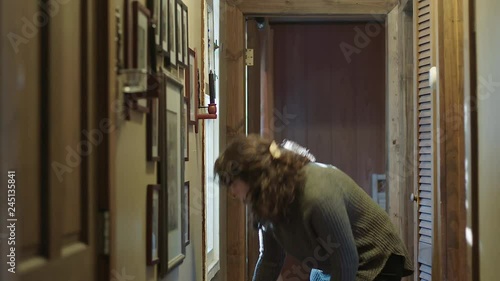 A young woman drills a hole for a nail to hang a framed photograph in her home.