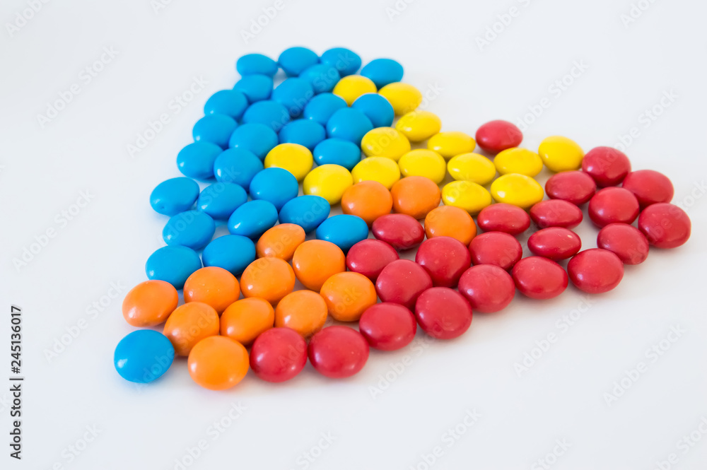 multicolored round candies dragees laid out in the shape of a heart on a white background multicolored round candies dragees laid out in the shape of a heart on a white background