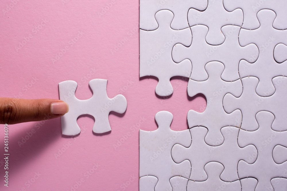 Close up of hand placing the last jigsaw puzzle piece on pink background. Business and team work concept. Close up of hand placing the last jigsaw puzzle piece on pink background. Business and team work concept.
