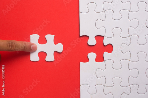 Close up of hand placing the last jigsaw puzzle piece on red background. Business and team work concept.