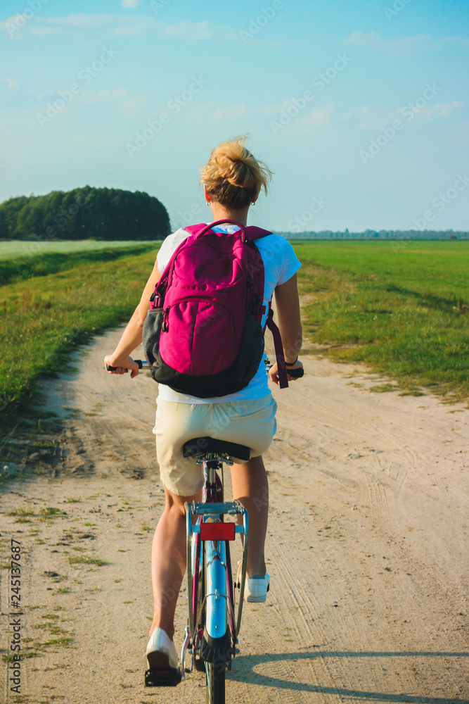 Fototapeta premium Young beautiful woman rides on a bicycle in the summertime on the green fields background