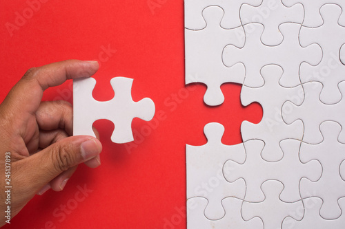 Close up of hand placing the last jigsaw puzzle piece on red background. Business and team work concept.