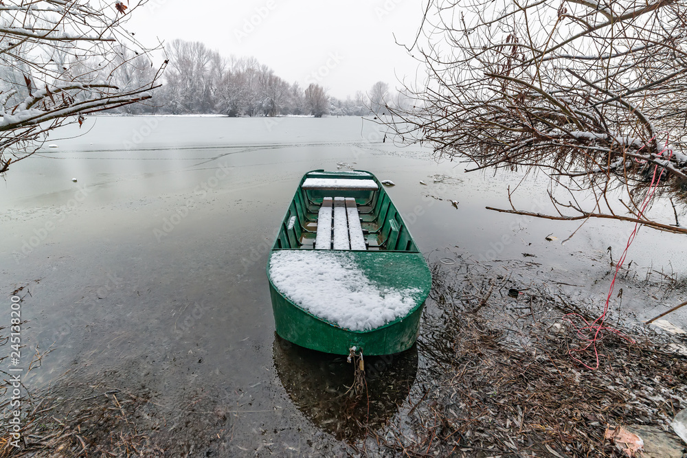 Naklejka premium Danube island (Šodroš) near Novi Sad, Serbia. Colorful landscape with snowy trees, beautiful frozen river. A boat covered with snow.