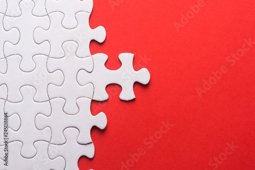 Unfinished white jigsaw puzzle pieces on red background