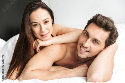 Caucasian couple man and woman kissing together, while lying in bed at home or hotel apartment