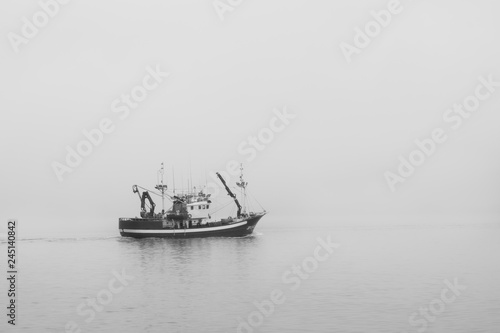 Fishing boat in the sea under the clouds and fog. Black and white photo