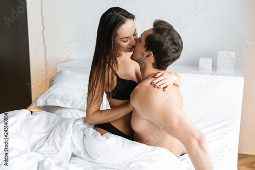 Attractive couple 30s making love, while lying in bed at home or hotel apartment