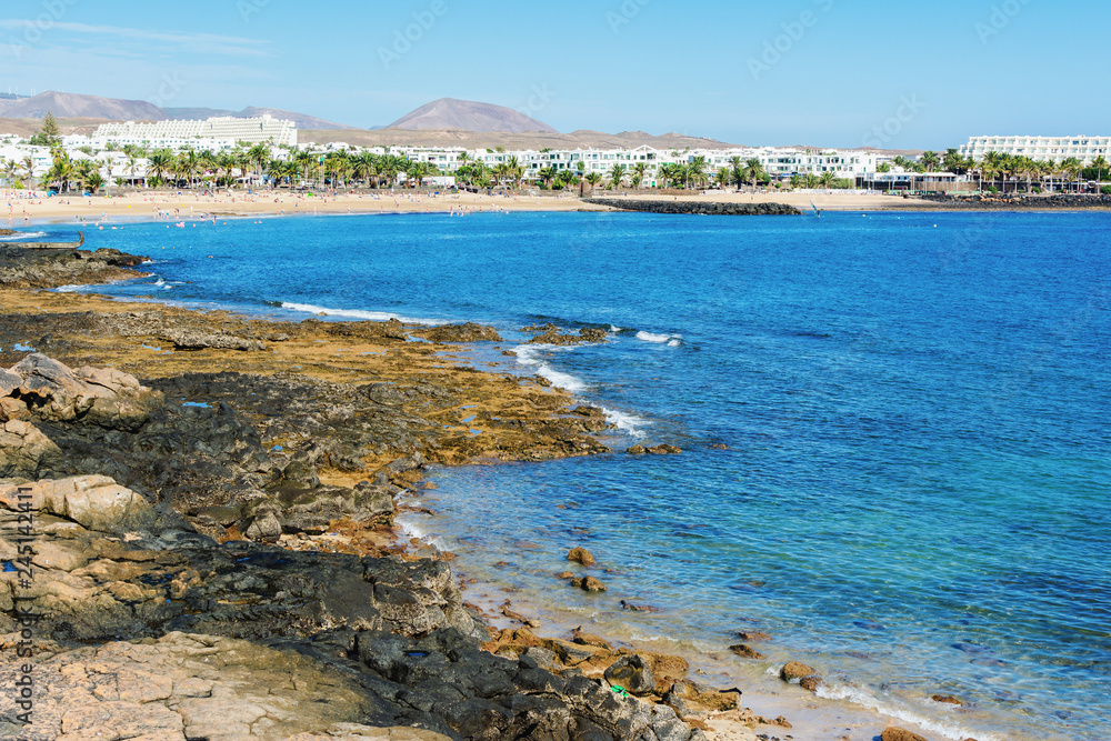 Golden sand and volcanic rocks at Las Cucharas beach, Lanzarote, Canary islands. VIew of the sea, coast and rocks, selective focus