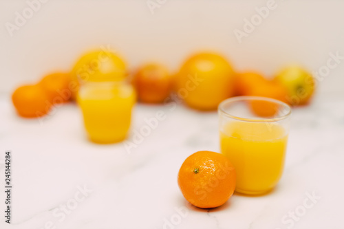 healthy fruit including oranges grapefruits and apples scattered on light-toned marble and with juice glasses