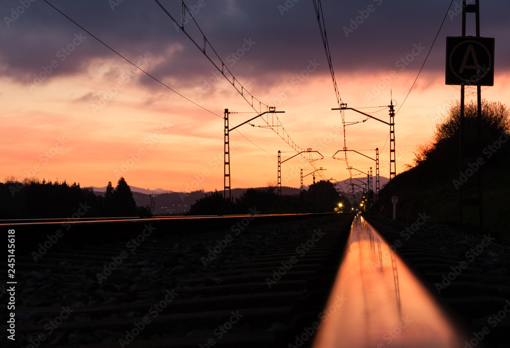 Railway station against beautiful sky at sunset. Industrial landscape with railroad, colorful blue sky with red clouds, sun