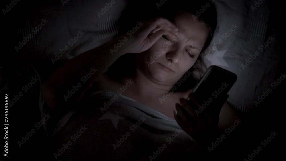 Beautiful young Woman Lying in Bed, Using Smart Phone and Smiling before Sleep. Woman using Cellphone on bed at Night. Attractive Girl looking at Mobile Phone. Beautiful young Woman Lying in Bed, Using Smart Phone and Smiling before Sleep. Woman using Cellphone on bed at Night. Attractive Girl looking at Mobile Phone.
