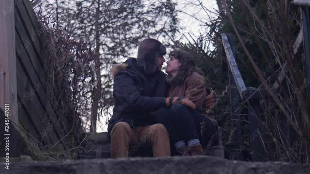 Young romantic couple hide away & kiss on secluded steps at dusk, rural setting Young romantic couple hide away & kiss on secluded steps at dusk, rural setting