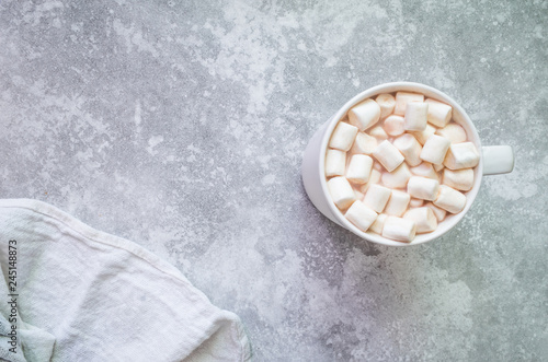 Cup of cocoa with marshmallows and white dishcloth on gray background