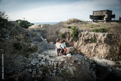 poor kids orphans sitting on ruins of destroyed house in war conflict area at Middle East