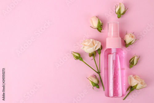 cosmetics for face and body in pink bottles with fresh roses on a delicate pink background. view from above. space for text