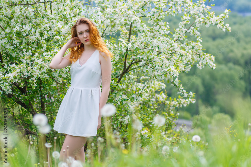 Beautiful and young girl standing next to a blooming Apple tree in a white dress. Red lips of the girl. Beautiful and young girl standing next to a blooming Apple tree in a white dress. Red lips of the girl.