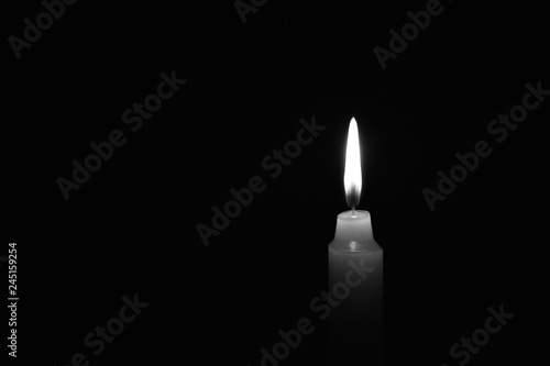 Candle burning in the black background. Black and white photo. Located on the right side of the shot.