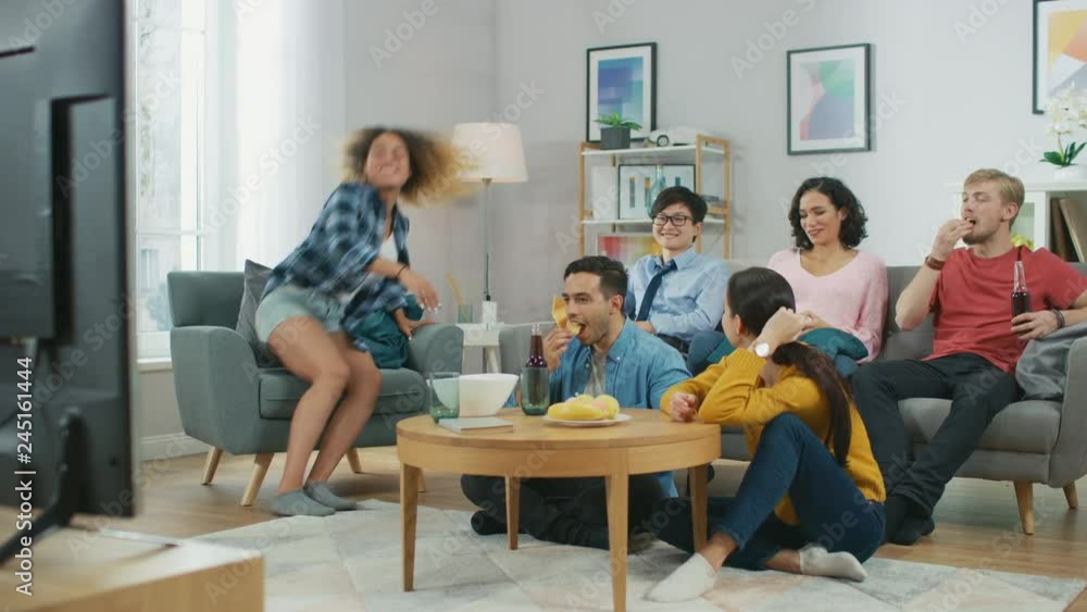 At Home Diverse Group Friends Watching TV Together, Eating Snacks and Drinking Beverage. They Probably Watching Sports Game or Fun Movie. At Home Diverse Group Friends Watching TV Together, Eating Snacks and Drinking Beverage. They Probably Watching Sports Game or Fun Movie.
