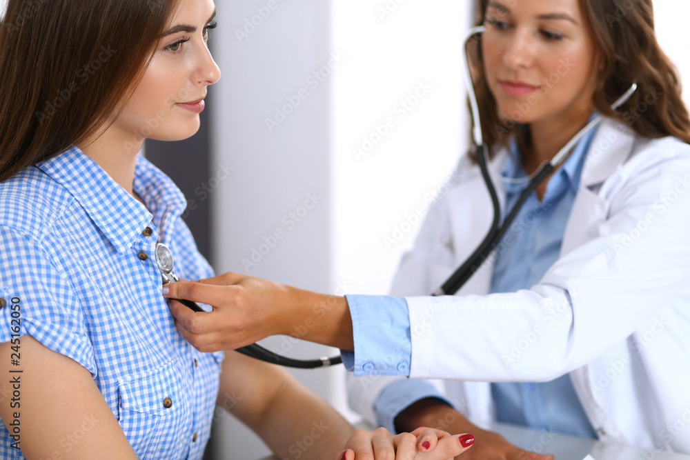 Doctor with a stethoscope in the hand examining her female patient. Health care, cardiology and medicine concepts Doctor with a stethoscope in the hand examining her female patient. Health care, cardiology and medicine concepts
