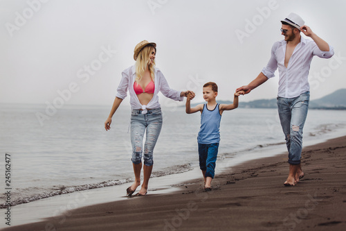 Mother and father with their son walking together on a quiet beach.