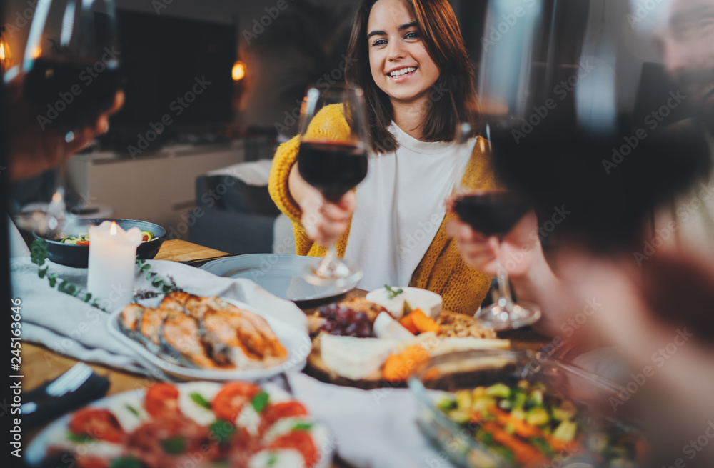 Best friends making cheers with glasses of red wine during dinner at home, Healthy Food Celebrate Dinner Concept, group of young hipsters enjoying tasty food in cozy home interior