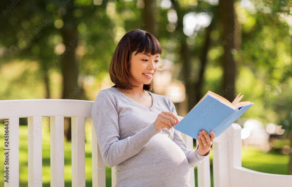 pregnancy, people and motherhood concept - happy pregnant asian woman sitting on park bench and reading book pregnancy, people and motherhood concept - happy pregnant asian woman sitting on park bench and reading book