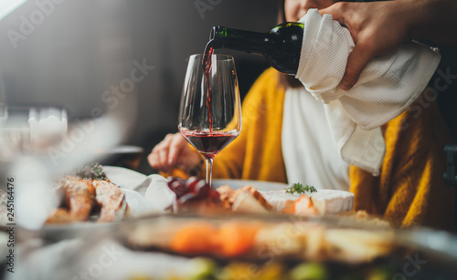 Romantic young caucasian man pouring red wine for his girlfriend during dinner date at restaurant enjoying healthy food, romantic atmosphere, happy couple celebrating concept