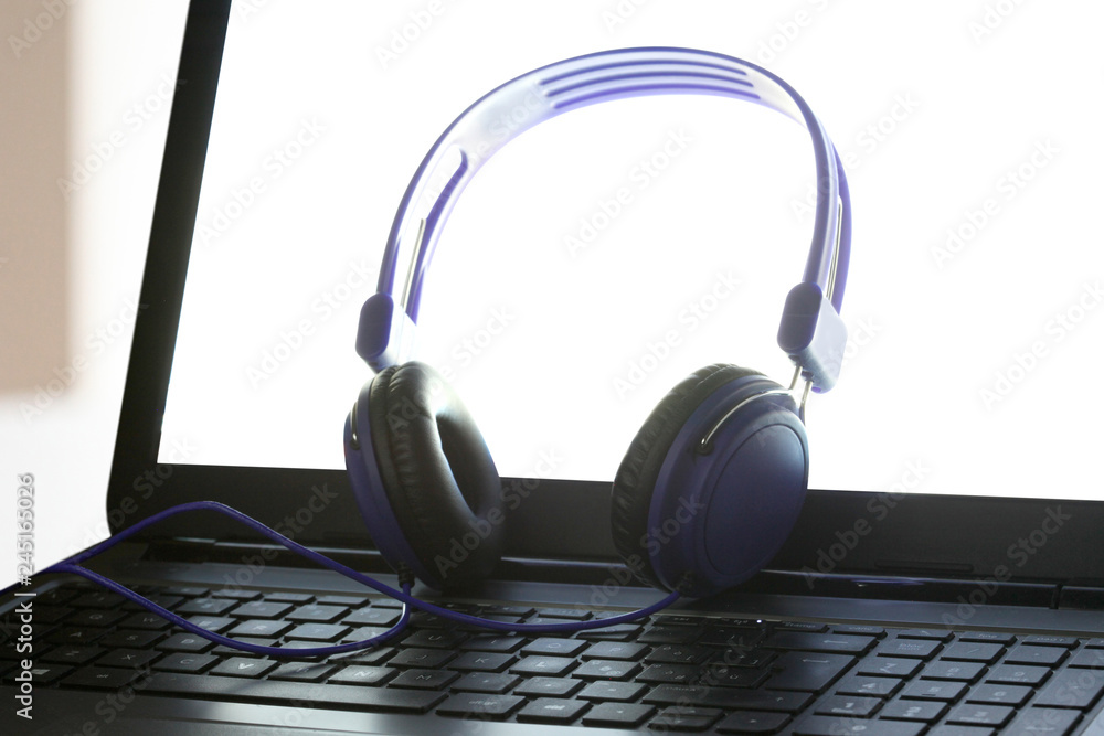 blue headphones rest on a laptot computer with cliipng path on the pc screen and copy space blue headphones rest on a laptot computer with cliipng path on the pc screen and copy space