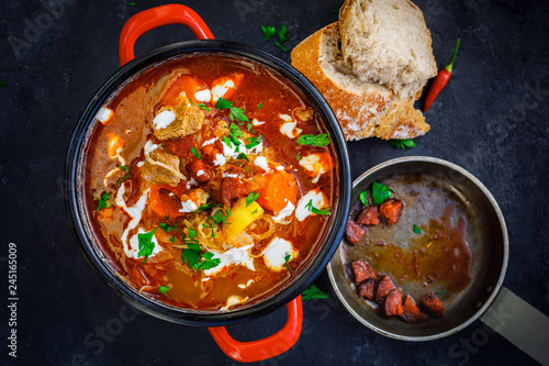 goulash soup in red pot and bread slices on rustic black board background