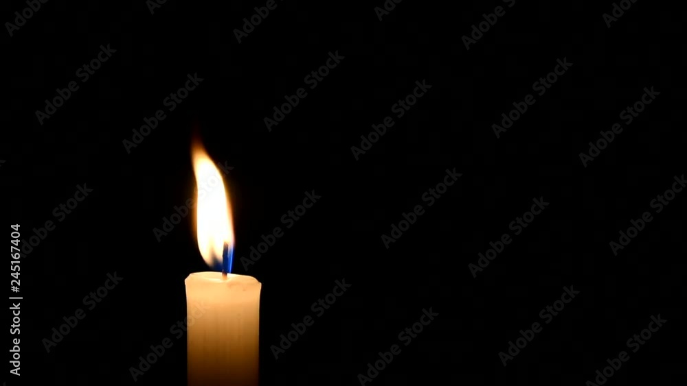 The wind is blowing on the candle flame. Black background. There`s room for your text. The concept of mourning, grief or sorrow. Located on the left side of the shot. The wind is blowing on the candle flame. Black background. There`s room for your text. The concept of mourning, grief or sorrow. Located on the left side of the shot.