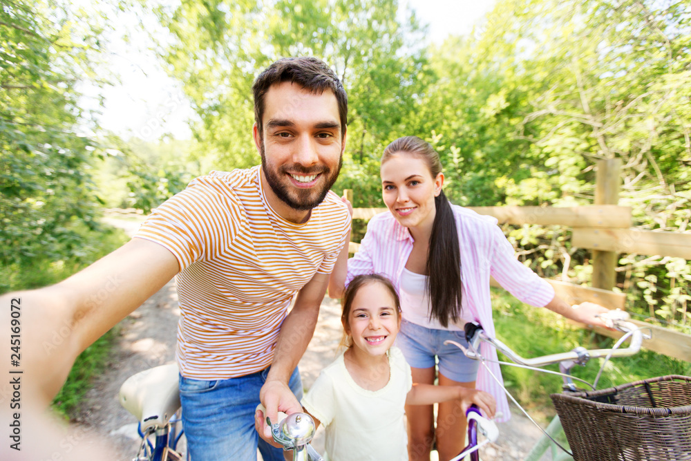 family, leisure and people concept - happy mother, father and little daughter with bicycles taking selfie in summer park family, leisure and people concept - happy mother, father and little daughter with bicycles taking selfie in summer park