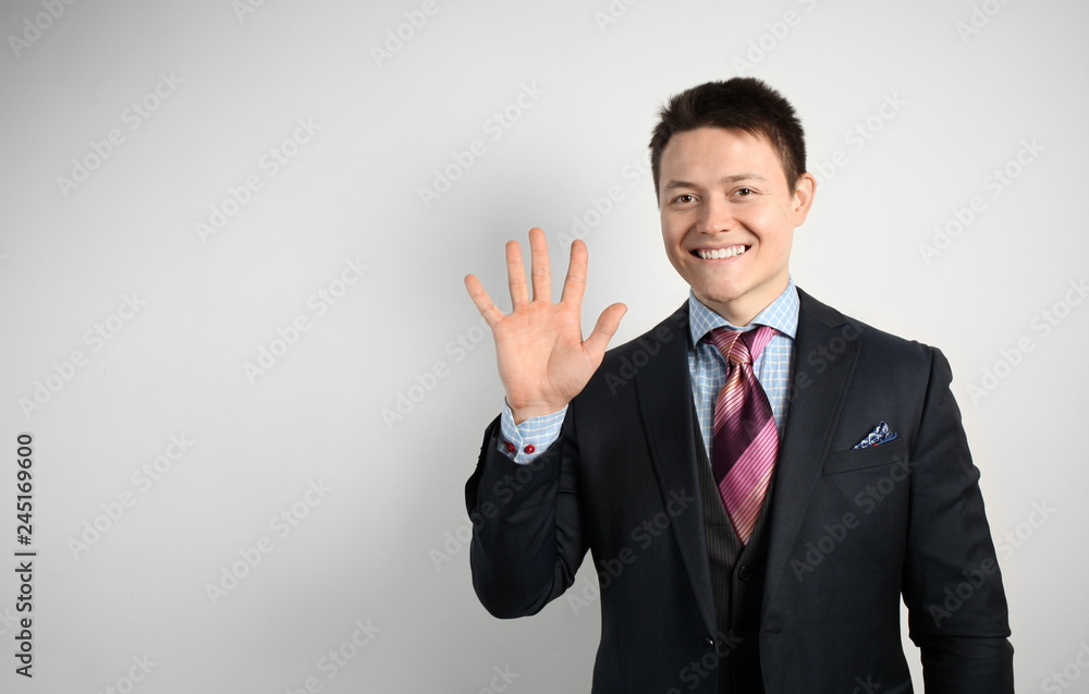 Young attractive businessman businessman in suit on gray background showing five fingers. Welcome gesture. Young attractive businessman businessman in suit on gray background showing five fingers. Welcome gesture.