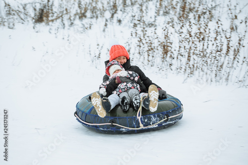 Happy mother and daughter having fun on slide with tube in winter