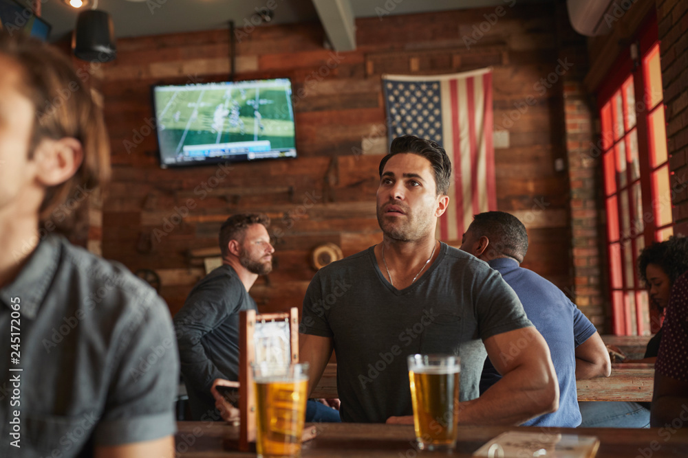Male Friends Drinking Beer And Watching Game On Screen In Sports Bar