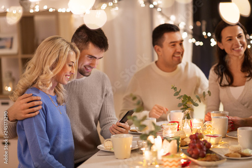 celebration, holidays and people concept - happy friends or family with smartphone having tea party at home