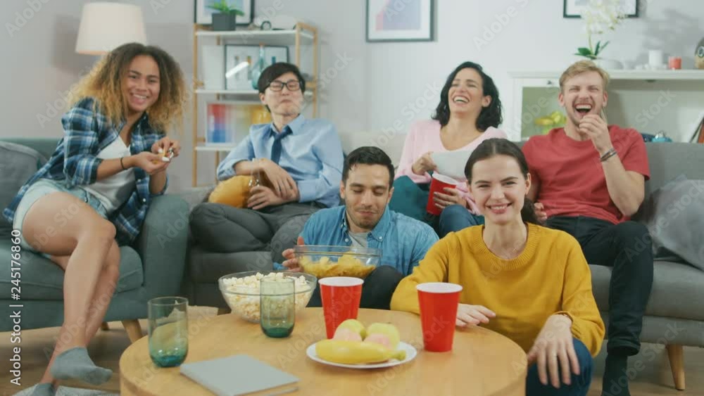 At Home Diverse Group Friends Watching TV Together, Eating Snacks and Drinking Beverage. Watching Comedy Sitcom or a Movie, Laughing and Having Fun Together.