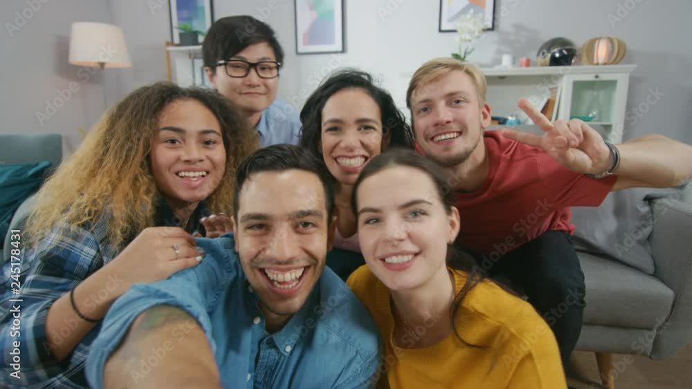 At Home Diverse Group of Friends Doing Collective Selfie, Guy Lifts Smartphone People Smile, Laugh and do Duck Lips.Young People Doing Live Stream of the Home Party. At Home Diverse Group of Friends Doing Collective Selfie, Guy Lifts Smartphone People Smile, Laugh and do Duck Lips.Young People Doing Live Stream of the Home Party.