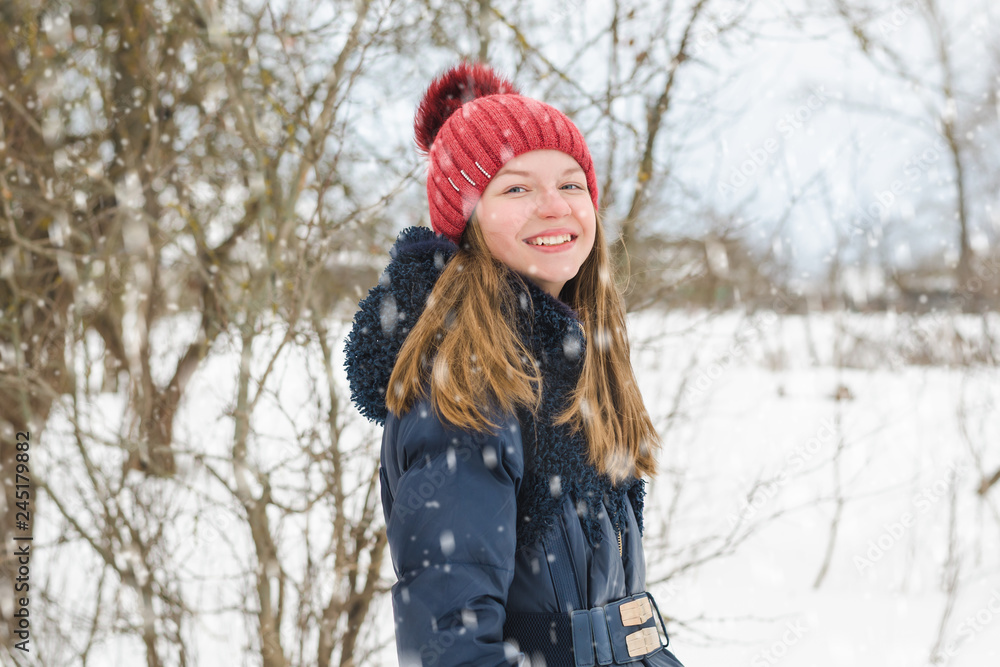 Young beautiful fair-haired girl stands and laughs in the park under soft fluffy snow on a cold winter day Young beautiful fair-haired girl stands and laughs in the park under soft fluffy snow on a cold winter day