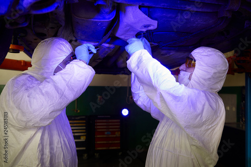 Crime investigation - collecting of evidences and traces from chassis of suspected car in police garage under UV light photo