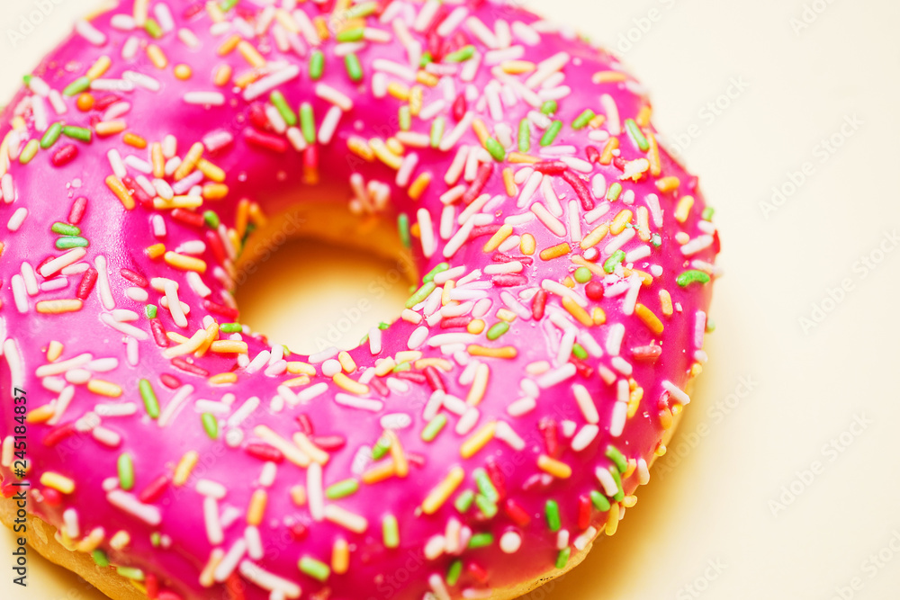 Bright donut in a pink glaze with a multi-colored rainbow sprinkle on a yellow background. Bright donut in a pink glaze with a multi-colored rainbow sprinkle on a yellow background.