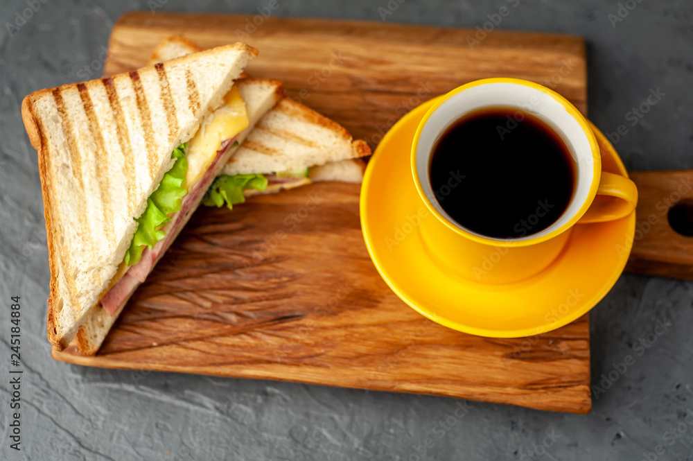 two delicious sandwiches with ham, cheese, lettuce and a cup of coffee on a wooden background two delicious sandwiches with ham, cheese, lettuce and a cup of coffee on a wooden background