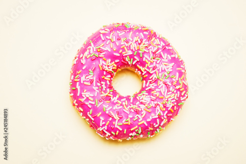 Bright donut in a pink glaze with a multi-colored rainbow sprinkle on a yellow background. 