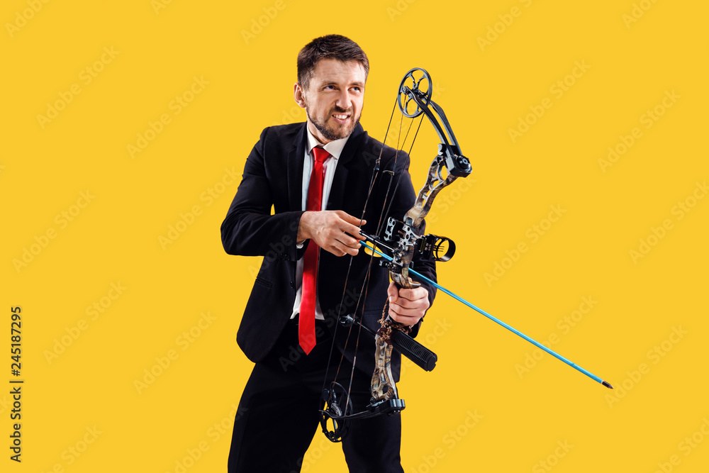 Fototapeta premium Businessman aiming at target with bow and arrow, isolated on yellow studio background. The business, goal, challenge, competition, achievement concept