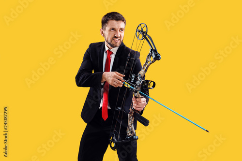 Businessman aiming at target with bow and arrow, isolated on yellow studio background. The business, goal, challenge, competition, achievement concept