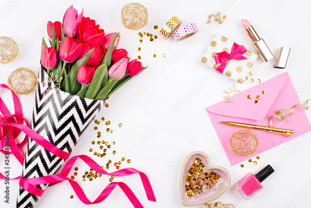 Pink and Gold Styled Desk with Florals. Pink tulips in black and white stylish wrapping paper, gifts, cosmetics and female accessories with confetti on white background Pink and Gold Styled Desk with Florals. Pink tulips in black and white stylish wrapping paper, gifts, cosmetics and female accessories with confetti on white background