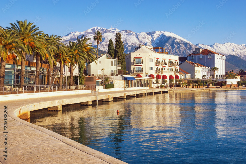 Beautiful Mediterranean landscape on sunny winter day. Montenegro, Bay of Kotor. Embankment of Tivat city and snowy peaks of Lovcen mountain