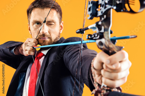 Businessman aiming at target with bow and arrow, isolated on yellow studio background. The business, goal, challenge, competition, achievement concept