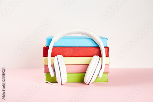 Electronic audiobook vs regular paper book concept. Stack of different color hardcover books with blank colorful covers & white headphones on table. Old versus new. Close up, copy space, background.
